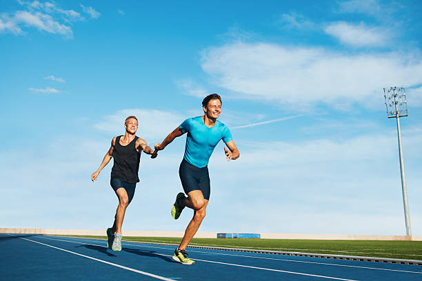 Athletes pass the baton in a track relay Shot of professional male athletes passing over the baton while running on the track. Athletes practicing relay race on racetrack. relay photos stock pictures, royalty-free photos & images