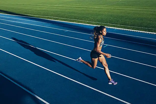 Outdoor shot of young African woman athlete running on racetrack. Professional sportswoman during running training session.