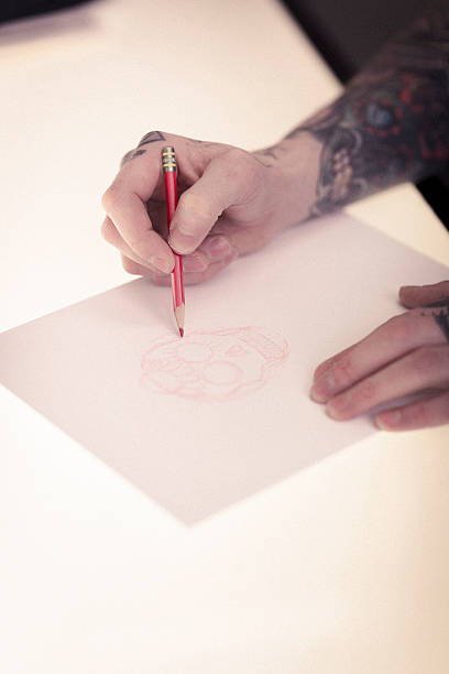 istock Artist's tattooed hands drawing skull on paper in studio 489305024