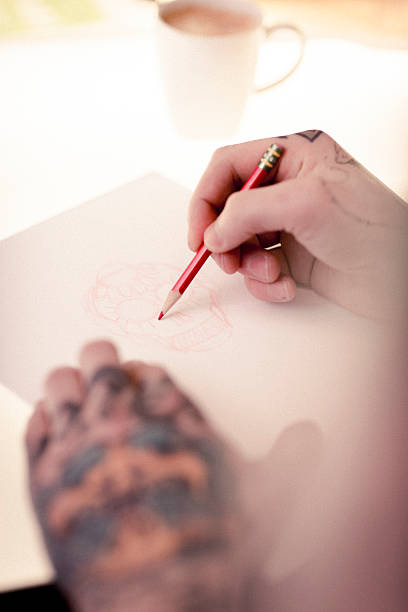 istock Artist's tattooed hands drawing skull on paper 489305120