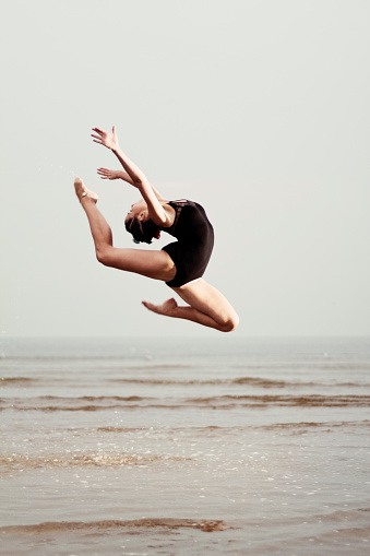 Young female gymnast jumping over sea surface.