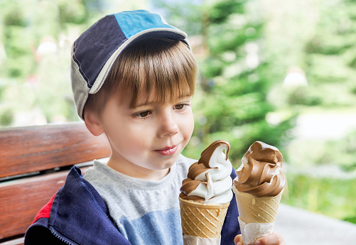 Ice cream cone  - yummy! Cute boy with two delicious ice cream on green background. Little child (toddler, kid) will eat tasty ice-cream in the sunny day. Caucasian male model. Food, summer, travel concept. Copy space.