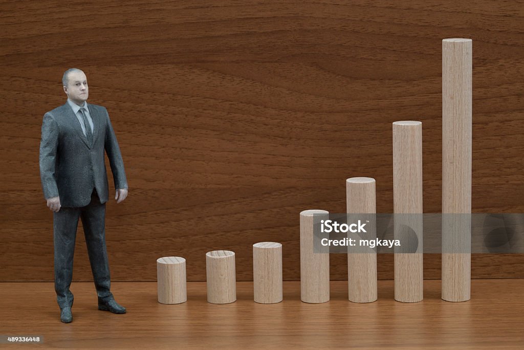 Businessman Action Figure and Wooden Bar Chart Businessman action figure and increasing cylinder bar chart made with wooden blocks on shelf. 2015 Stock Photo
