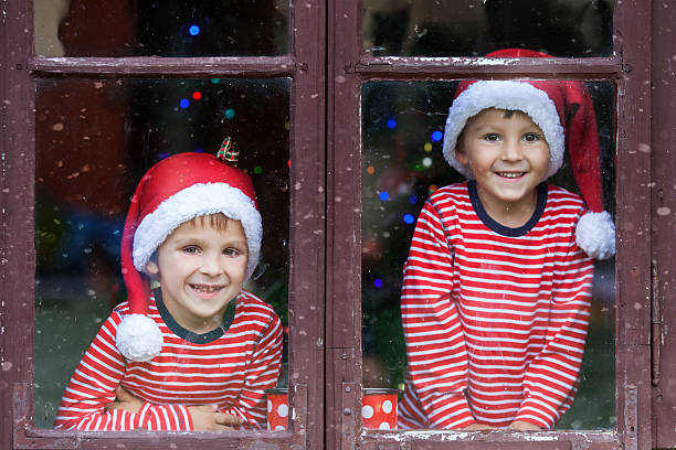 Two cute boys, brothers, looking through a window, waiting impatiently for Santa