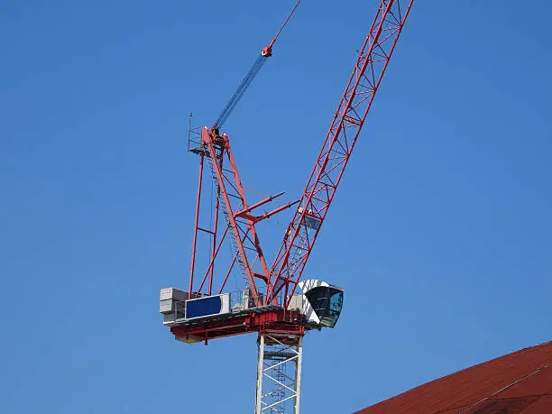 Photo showing a red tower crane that is working on a building construction site, where it is being used to move heavy objects.