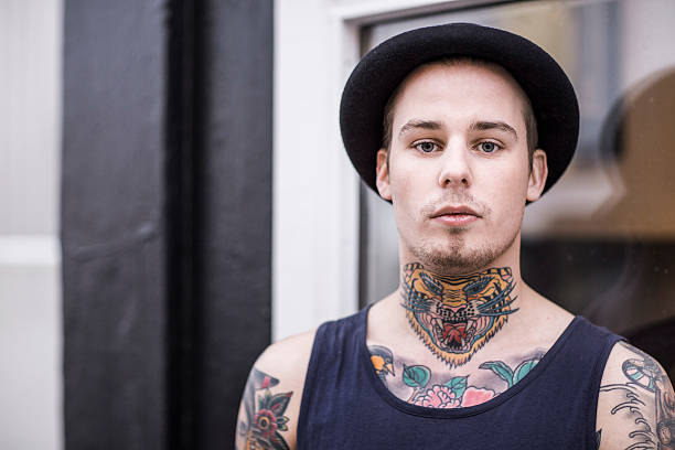 Young tattooed man outdoors A photo of young tattooed man outdoors. Portrait of fashionable male wearing hat and tank top. Confident hipster is with colourful tattoos. chest tattoos for men designs stock pictures, royalty-free photos & images