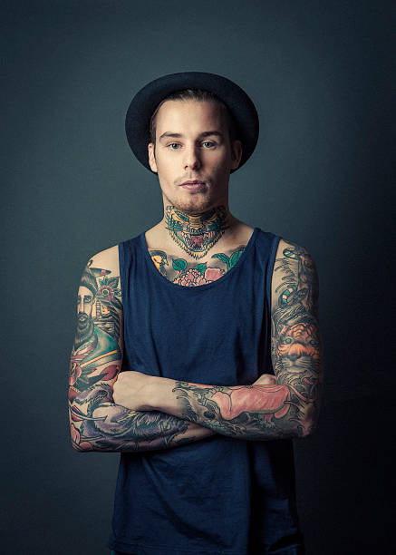Confident tattooed man with arms crossed A photo of confident tattooed man with arms crossed. Portrait of fashionable male standing against grey background. Hipster is with colourful tattoos. chest tattoos for men designs stock pictures, royalty-free photos & images