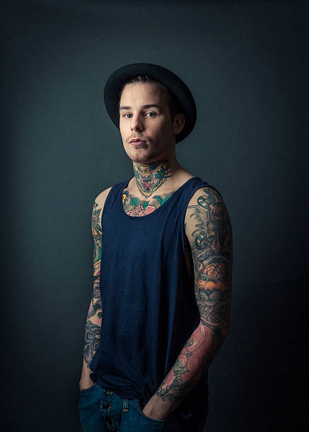 Confident tattooed man with hands in pockets A photo of confident young tattooed man standing with hands in pockets. Portrait of fashionable male standing against grey background. Confident hipster is with colourful tattoos. chest tattoos for men designs stock pictures, royalty-free photos & images