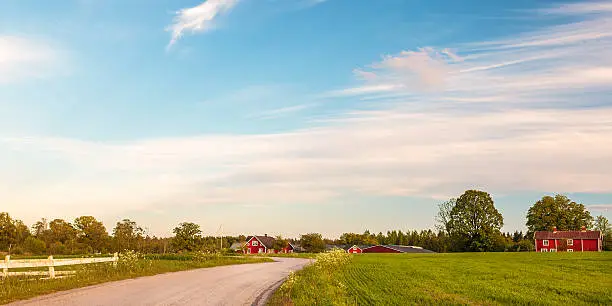 Panoramic image of old red wooden farms with road during sundown in Smaland, Sweden