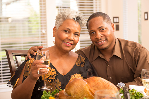 African descent adult son and his mother make a toast during a family holiday dinner.  Thanksgiving or Christmas meal together.  A roasted turkey is in front of the couple on the dining room table. 
