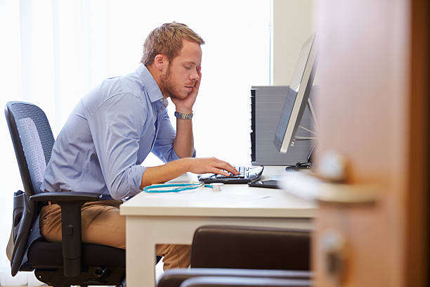 istock Overworked Male Doctor In Office Sitting At Computer 489346776
