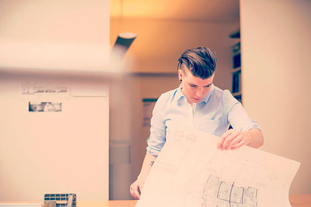 istock Female architect examining blueprint at desk at office 489347490