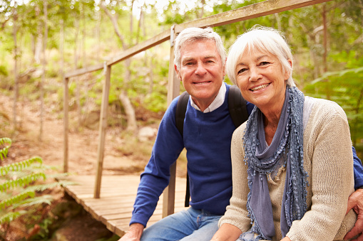 Happy senior couple sitting on a bridge in forest, portrait