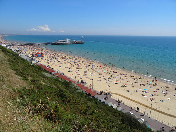Photo showing the busy seafront of Bournemouth beach.  This aerial view shows the pier in the distance, being pictured during the sunny summer holidays.