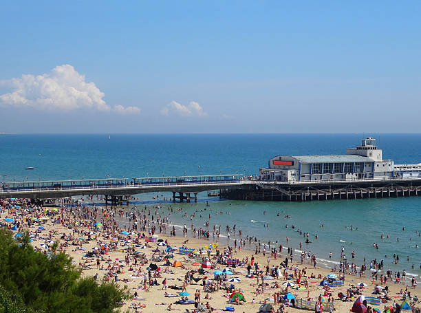 Photo showing the seafront of Bournemouth during the summer holiday season, when the beach is filled up with sunbathing tourists.