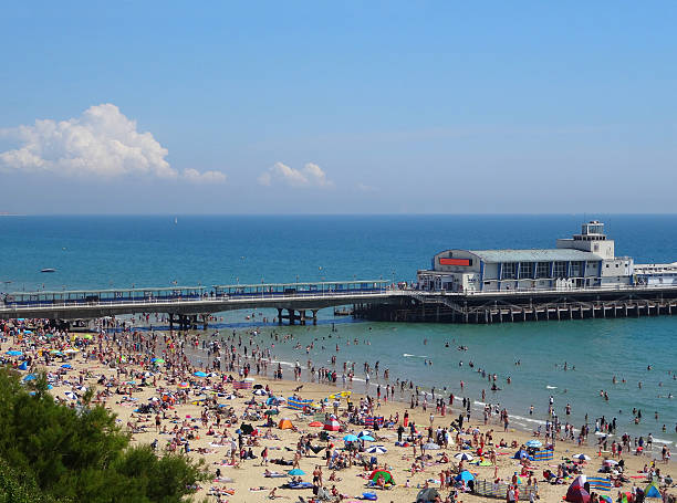 Image of Bournemouth beach and seafront with summer holidaymakers, pier Photo showing the seafront of Bournemouth during the summer holiday season, when the beach is filled up with sunbathing tourists. bournemouth england photos stock pictures, royalty-free photos & images