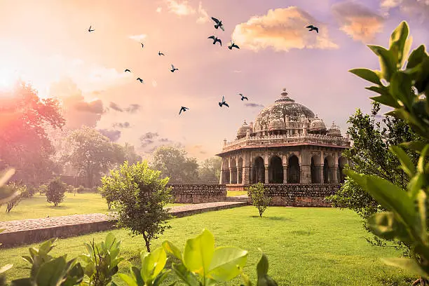 Early mooring Sunrise view of the Tomb of Isa Khan at Humayun’s Tomb complex. Birds flying in the colourful sky.