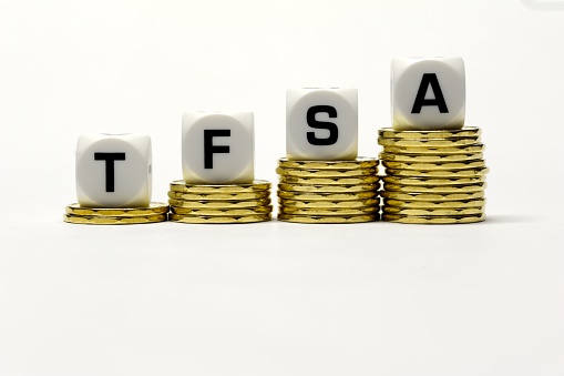The letter dice TFSA which represent the words Tax Free Saving Account placed on an ascending row of Canadian dollar coins representing the accumulation of tax free wealth over time. 
