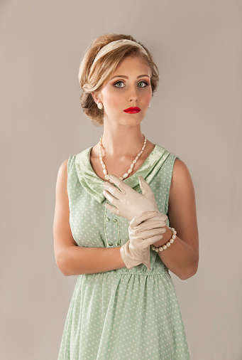 Color image of a beautiful blonde woman with a retro hairstyle with hairband, vintage leather gloves, fifties style green dress, with dots, fifties makeup and pearl jewelry