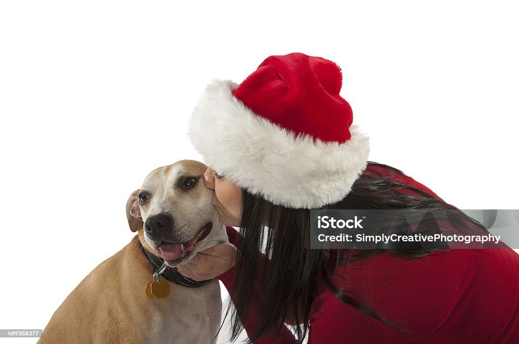 Woman with Santa Hat Kissing Dog A young woman kissing her dog while wearing a santa hat. Adult Stock Photo