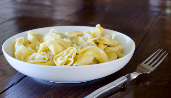 A bowl of freshly cooked tortelloni on a wooden table with a fork
