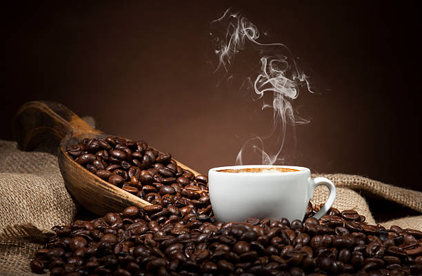 White cup with coffee beans on dark background White coffee cup and coffee beans on burlap textile and brown background. steam photos stock pictures, royalty-free photos & images