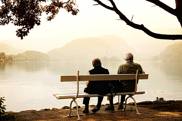 istock senior couple siting on bench at lake shore 489426679