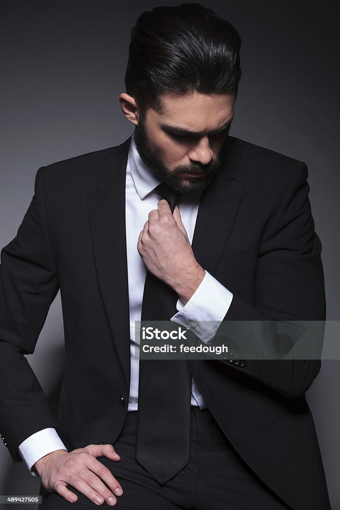 young fashion man looks down and fixes tie young fashion man looking down, away from the camera while adjusting his tie. on a dark background Men Stock Photo