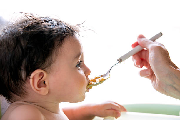 baby eats pasta from the spoon stock photo