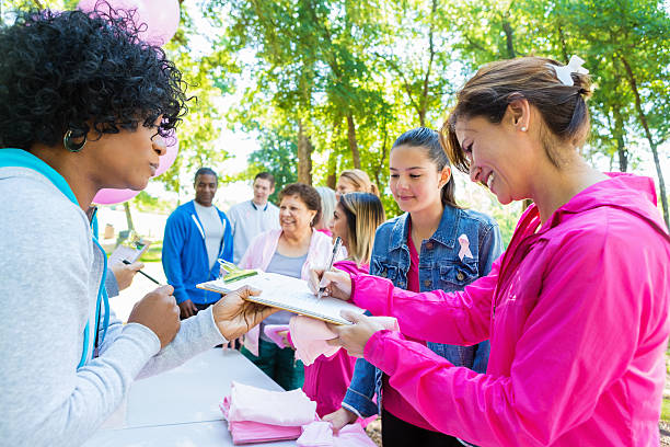 Diverse people registering for charity breast cancer awareness race Diverse group of adults and teenagers are lined up at registration table in sunny park. They are signing up to run in charity 5k race or marathon to raise money for breast cancer research. People are wearing pink athletic clothing and breast cancer awareness ribbons. registration form photos stock pictures, royalty-free photos & images