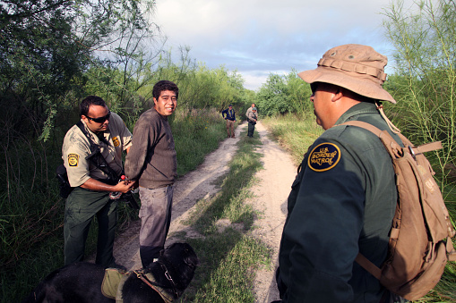 La Paloma, Texas, USA - September 22, 2015:  A  Border Patrol agent accompanied by his tracking dog transfers an illegal Mexican alien who has recently come ashore to another agent near the Rio Grande River.  Such encounters are a daily experience in the Rio Grande Valley sector of Border Patrol operations.