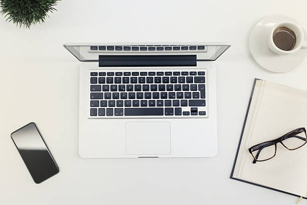 Place Of Work Nis, Serbia - August 15, 2015: Modern work place. Directly above view of laptop computer (MacBook Pro), notebook, eyeglasses, espresso coffee, mobile phone and money tree on the employee's working table at the business office.  apple keyboard stock pictures, royalty-free photos & images