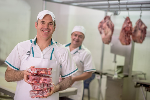 Happy men working at the butchery packing the meat