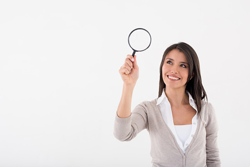 Business woman searching with a magnifying glass and looking happy - over a white background