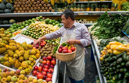 Business owner organizing fruits at a grocery store and holding a basket - personal shopper