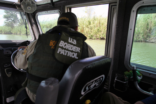 La Paloma, Texas, USA - September 22, 2015:  A Border Patrol agent pilots a river patrol boat and monitors the Rio Grande River for illegal aliens crossing into the U.S.  Such encounters are a daily experience in the Rio Grande Valley sector of Border Patrol operations.