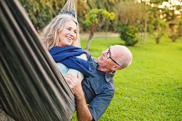 Senior european couple talking lying downin a hammock european senior man and senior women lying down  and playing in a hammock on the nature hammock relaxation women front or back yard stock pictures, royalty-free photos & images