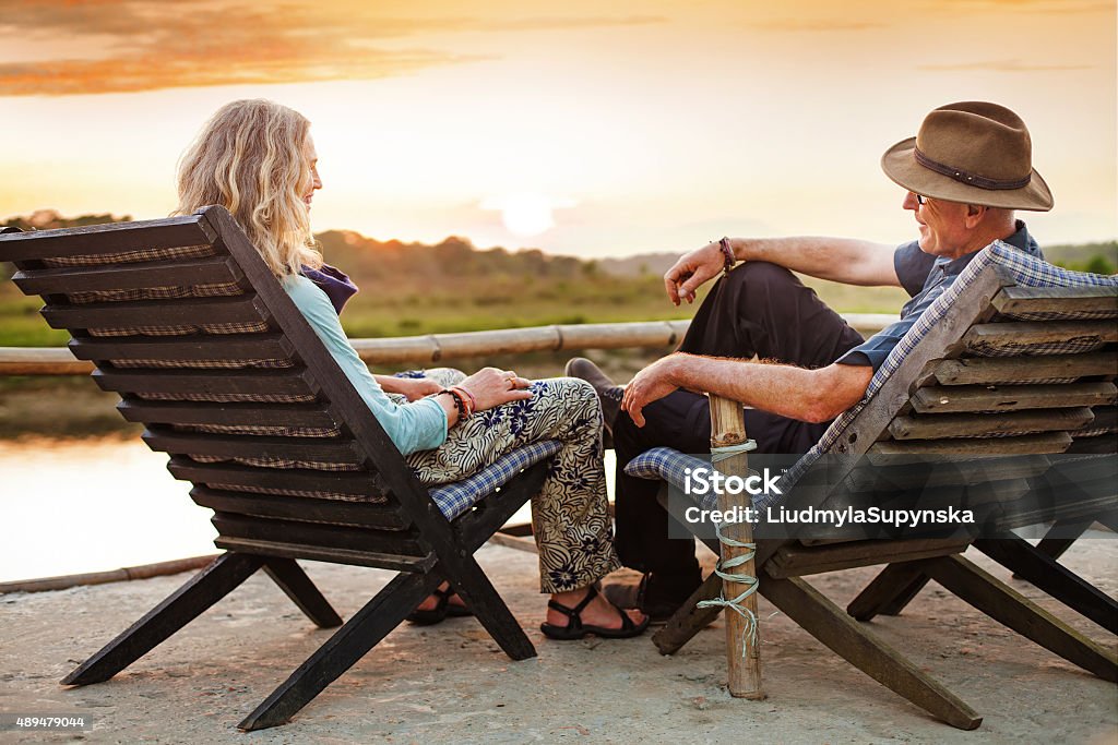 Senior european couple seating on chaise lounge on sunset adult man and adult woman relaxing in chaise lounge and talking Lake Stock Photo