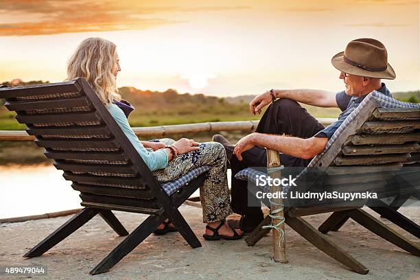 Senior European Couple Seating On Chaise Lounge On Sunset Stock Photo - Download Image Now