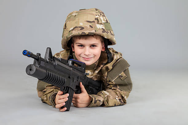 Young boy dressed like a soldier with rifle isolated on gray background
