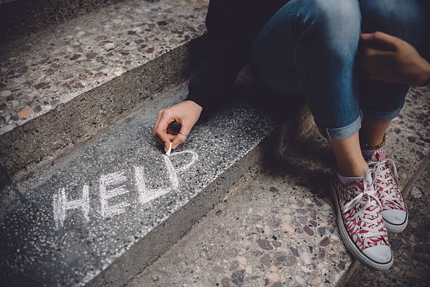 Unahppy girl writes help on the ground Teenage girl sitting on a staircase outside feeling depressed help single word stock pictures, royalty-free photos & images