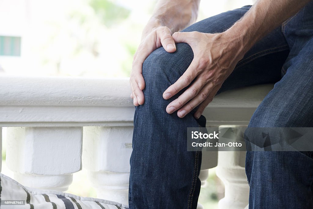 Knee pain A male person sitting on a balcony with sudden knee-pain.  Alternative Therapy Stock Photo