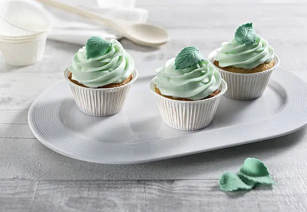 mint cupcakes trio on white serving dish with sugar mint-leaves decorations.