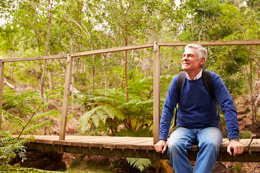 Senior man sitting alone on a wooden bridge in a forest