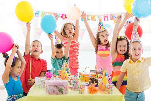 Large group of happy children celebrating birthday at birthday party with their arms raised.