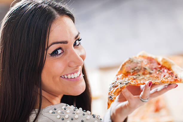 istock Young smiling woman eating pizza and looking at camera. 489515760
