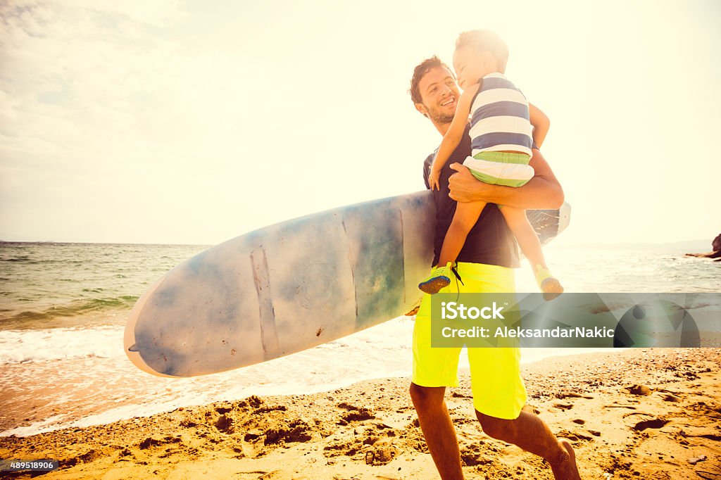 Let's find a good wave Photo of a surfer dad having fun at the beach with his little boy, teaching him to surf Beach Stock Photo