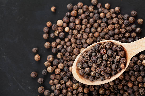 Closeup black pepper whole, copy space for your text Closeup black pepper whole in wooden spoon on black stone table, top view acrid taste stock pictures, royalty-free photos & images