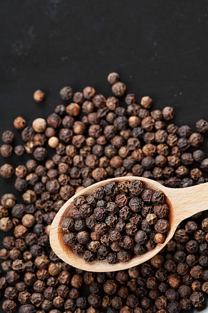 Black pepper whole with copy space for text, top view Closeup black pepper whole in wooden spoon on black stone table, top view acrid taste stock pictures, royalty-free photos & images