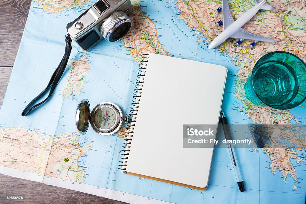 Travelling tools travel tourism agency table mockup tools compass, glass of water note pad, pen and toy airplane and touristic map on wooden table. Empty space you can place your text or information. Travel Stock Photo